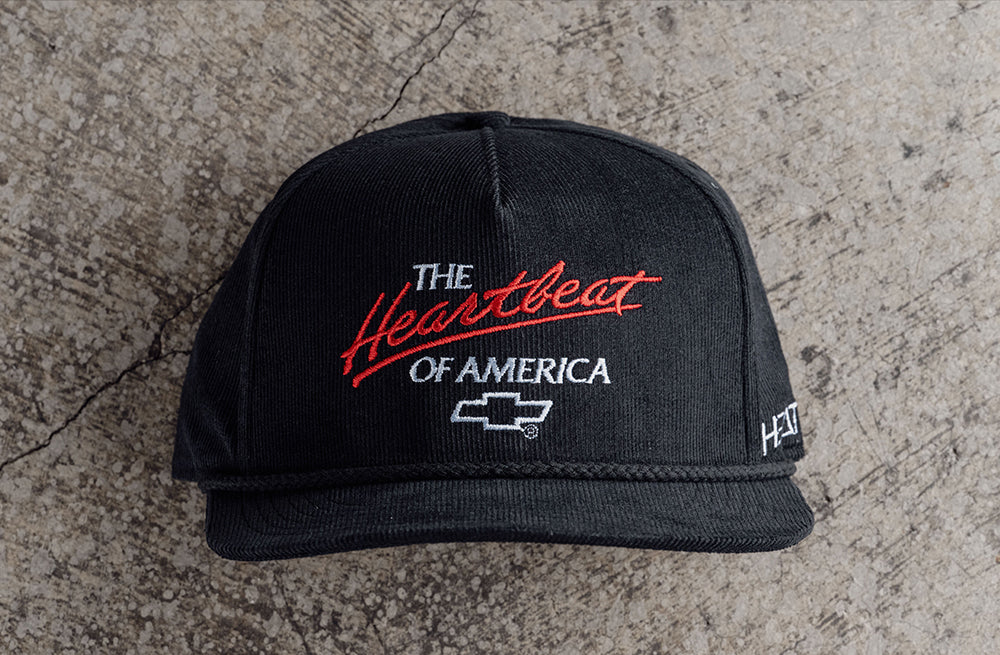 Lying face up on the concrete is the Heat Wave Visual X Chevrolet Heart Beat of America Black Corduroy Hat.