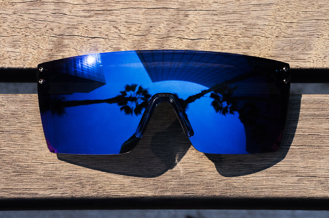 On a woodbench is the Heat Wave Visual Lazer Face Sunglassses with neon blue frame and coastal blue lens.