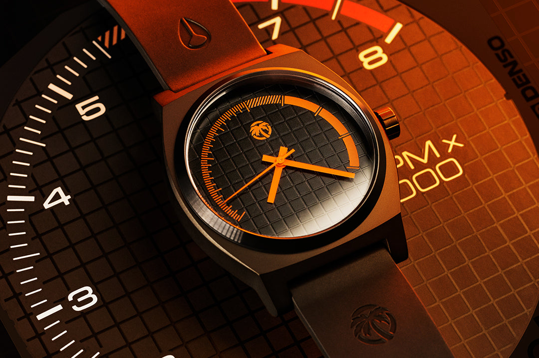 Lying on a tachometer is the Heat Wave Visual x Nixon Time Teller Watch.