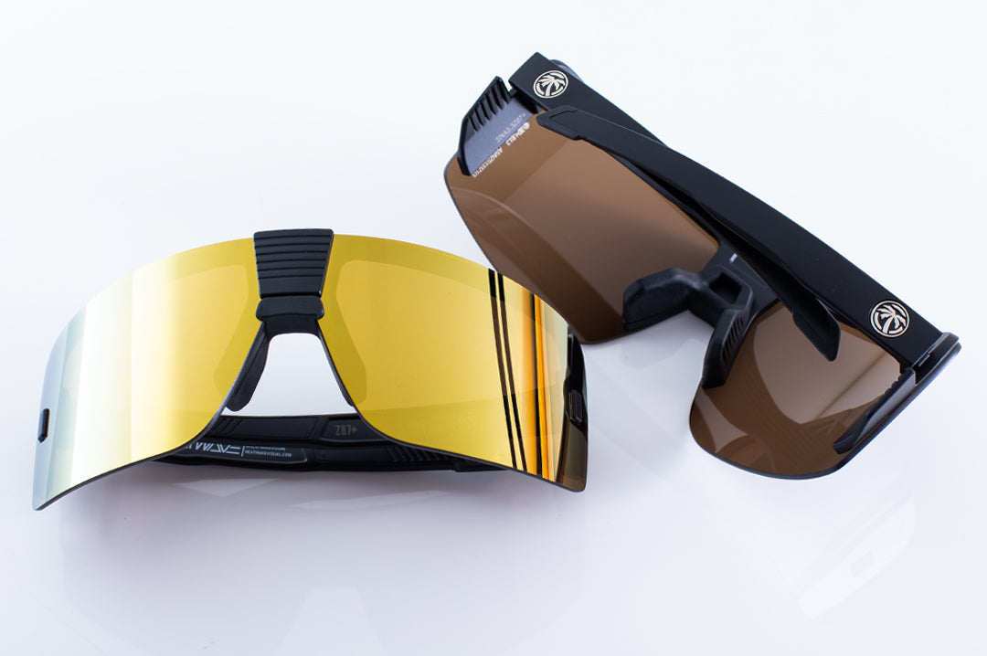 Two Heat Wave Visual Vector Sunglasses with black frame and gold lens lying on a table.