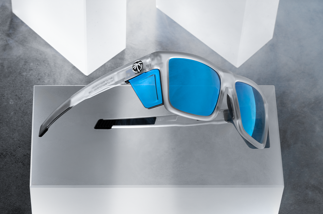 Indoor studio shot of the Performance Vise Sunglasses: Vapor Frost Frame Coastal Lens Z87+ with blue side shields on a concrete block.