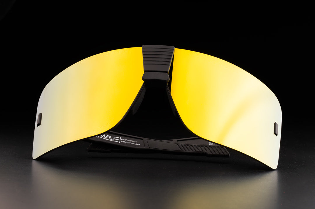 Lying on a table is the Heat Wave Visual XL Vector Sunglasses with black frame and gold lens.