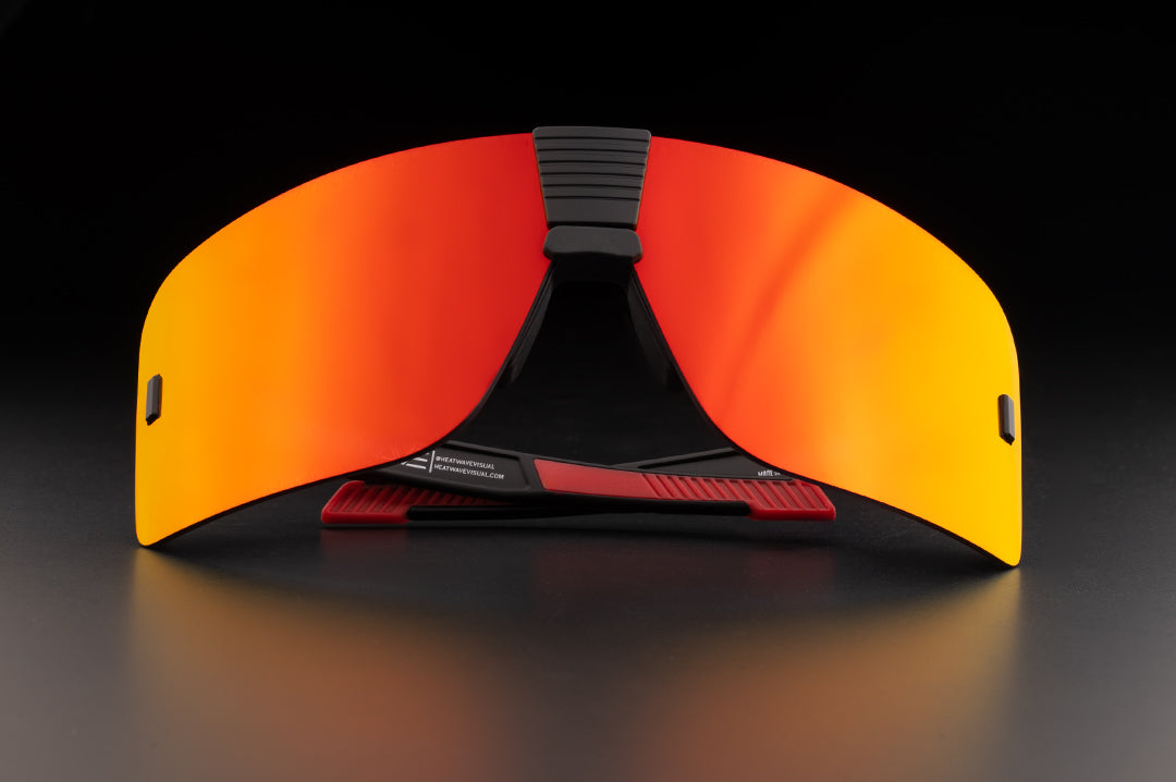 Lying on a table is the Heat Wave Visual XL Vector Sunglasses with black frame and firestorm red lens.