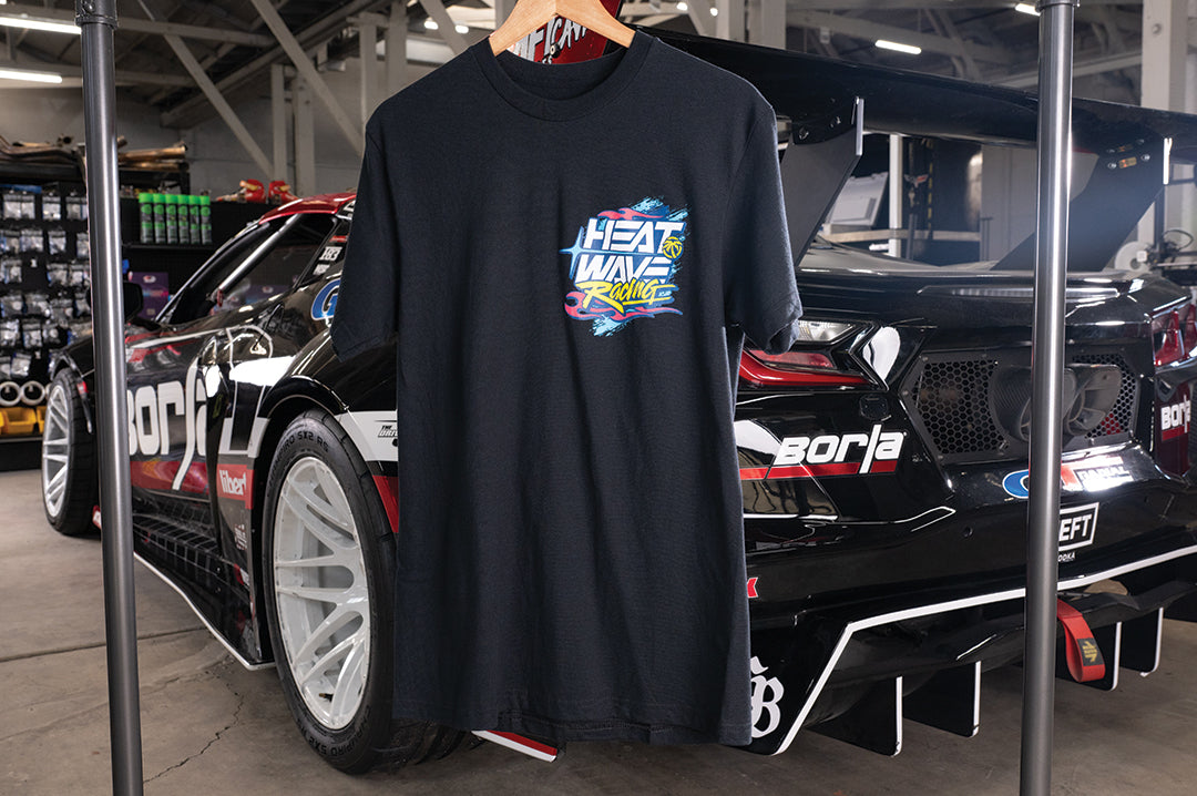 The Heat Wave Y2K Racing Black T-Shirt hanging in front of a car