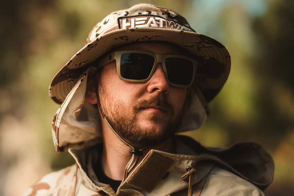 Man wearing a desert camo Heat Wave boonie hat and Vise than sunglasses with a blurred natural background