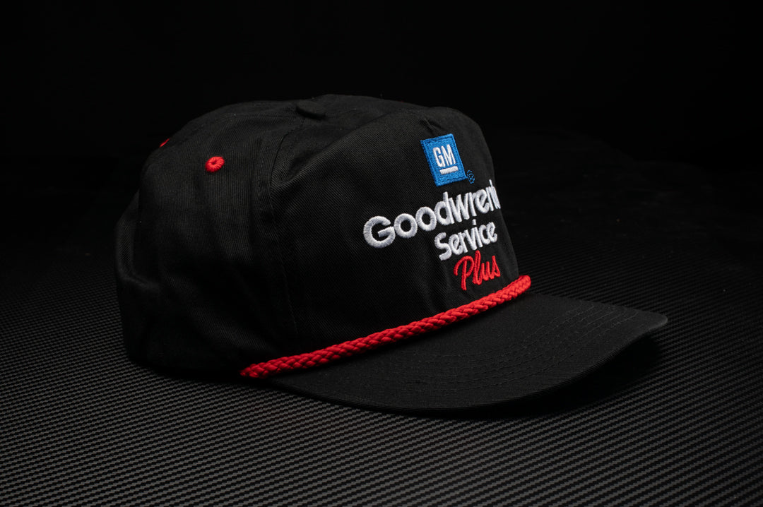 Laying on a table is the Heat Wave Visual GM Goodwrench hat in black.
