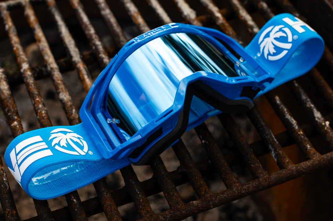Heat Wave Visual MXG 250 Motosport Goggle in the billboard icon arc flash blue color way lying on a grill. 