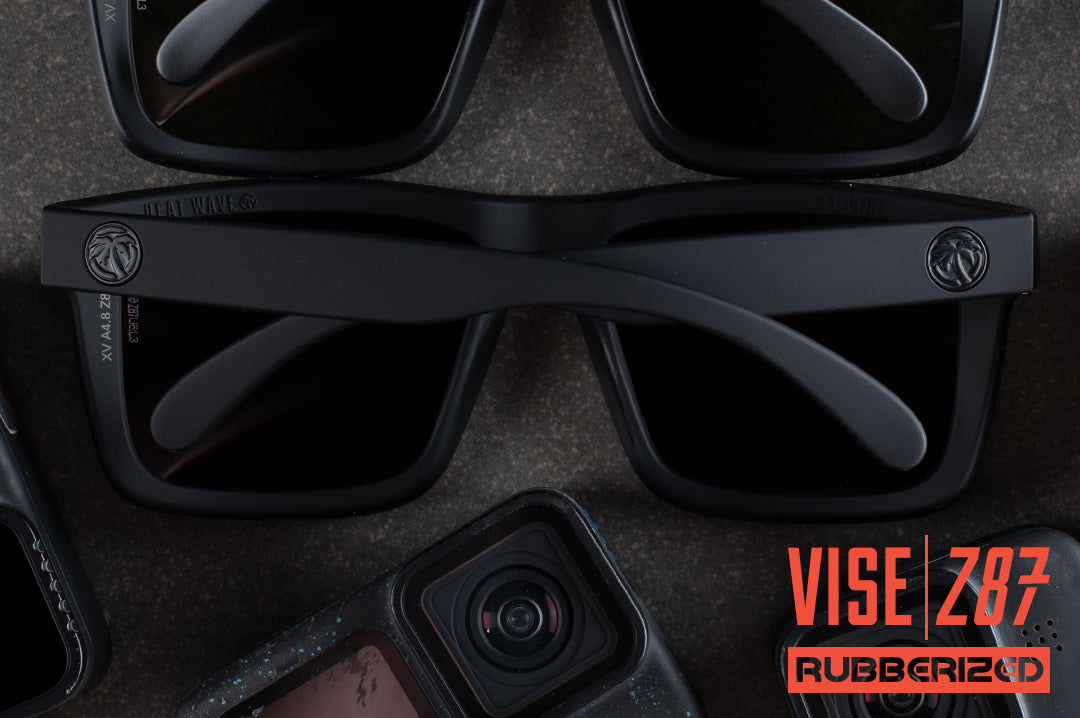  Laying on a table surrounded by gopros is the Heat Wave Visual Vise Z87 Sunglasses with rubberized frame and black lenses.