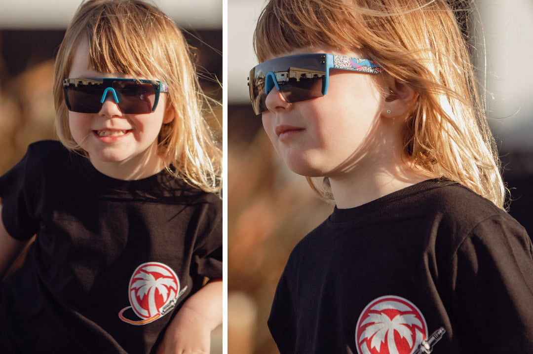 Toddler girl wearing Heat Wave Visual Lazer Face kids sunglasses blue frame, static print arms and black lens.