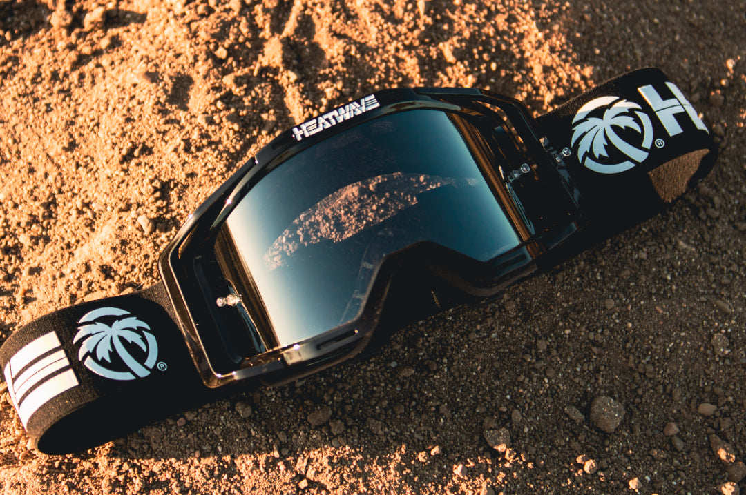 Heat Wave Visual MXG 250 Motosport Goggle in the billboard icon black color way laying on the dirt.