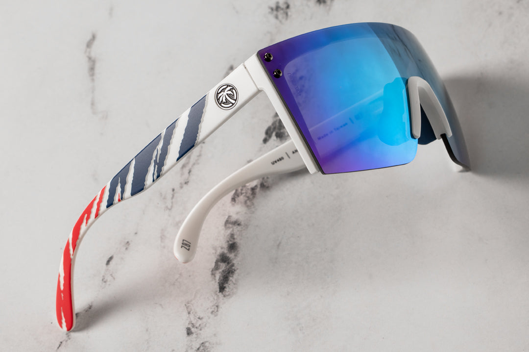 Side view on marble table of Heat Wave Visual Lazer Face Z87 Sunglasses with white frame, fireblade rwb print arms and galaxy blue lens.