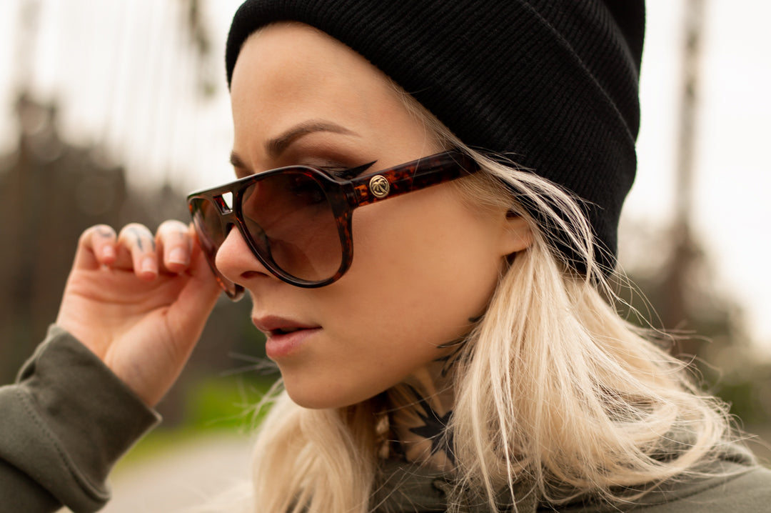 Close up of young woman wearing Heat Wave Visual Supercat Sunglasses with tortoise brown frame and brown lenses.