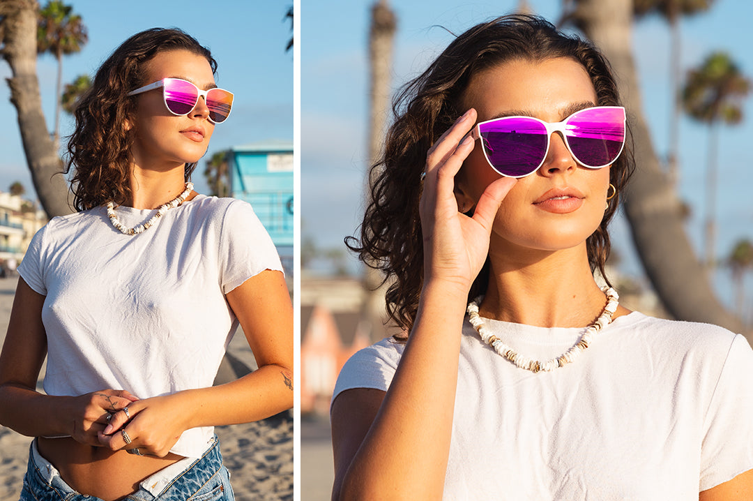 Young woman at the beach wearing Heat Wave Visual Womens Carat Sunglasses with white frame and spectrum pink lenses.