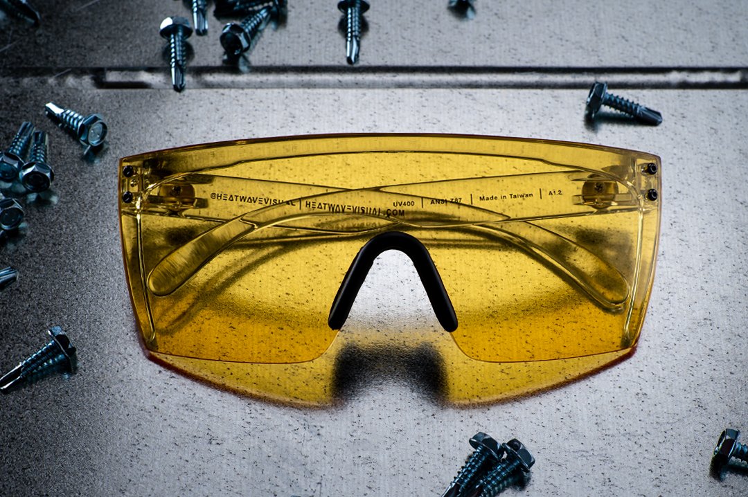 Heat Wave Visual Lazer Face Z87 Sunglasses with clear frame, black nose piece and hi-vis yellow lens on metal table surround by screws. 