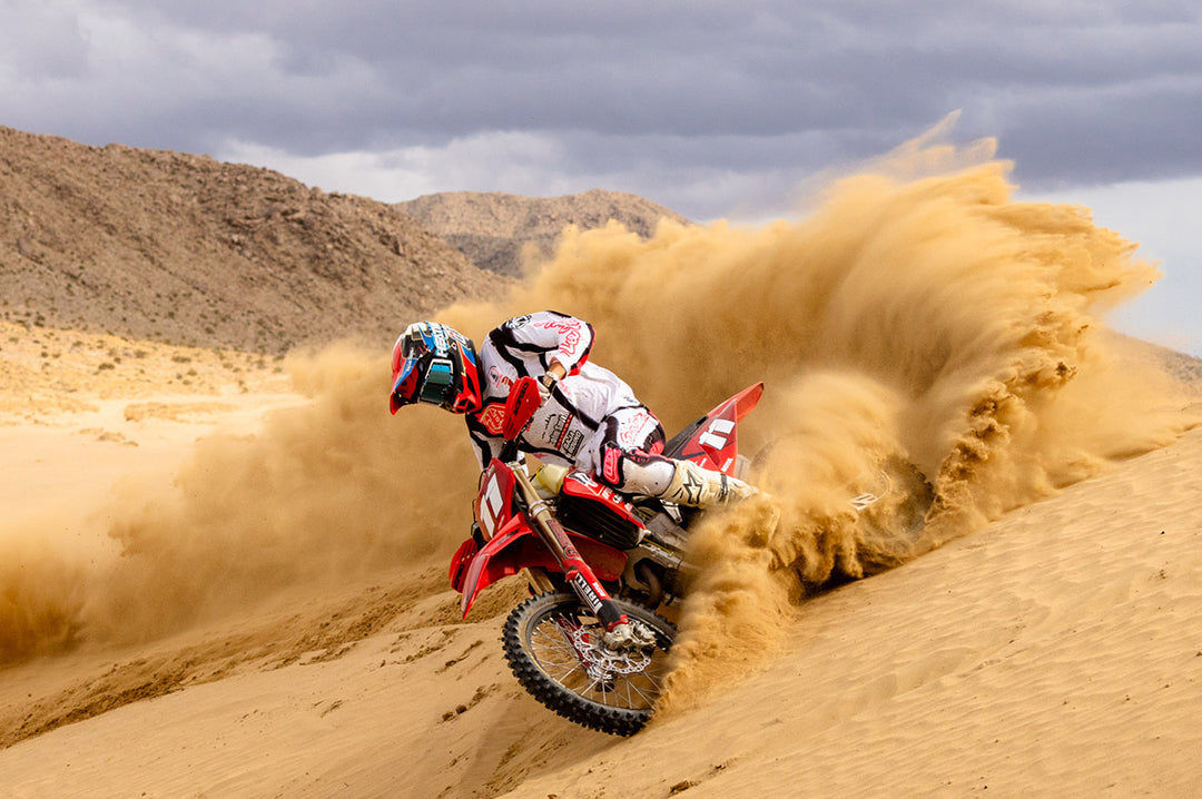 Action shot of a man riding a dirt bike in the desert wearing the Heat Wave Visual MXG 250 Motosport Goggle in the Lightning color way.
