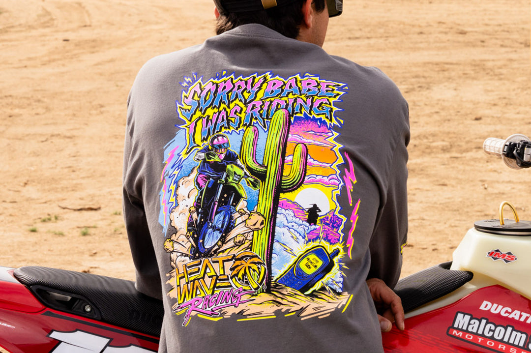 Man wearing the Heat Wave "Sorry Babe" LONG SLEEVE T-Shirt leaning on a dirt bike in the desert.