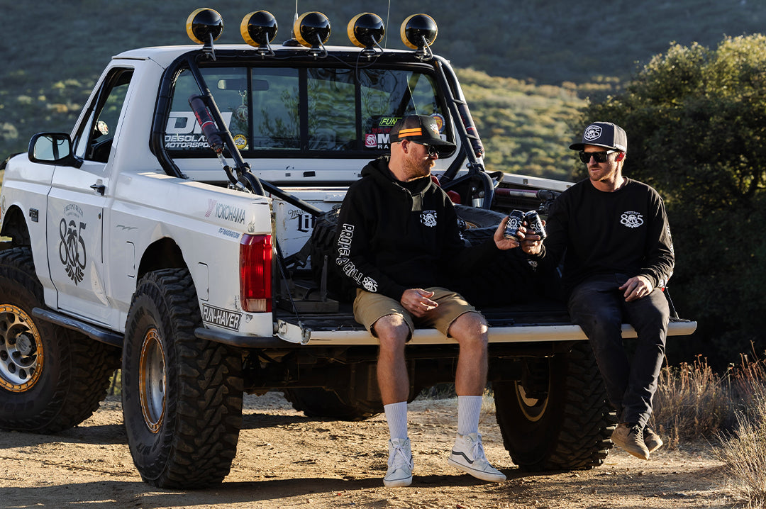Two men sitting on the truck bed wearing the Heat Wave x 805 Properly Chill Long Sleeve T-Shirt - Black drinking 805
