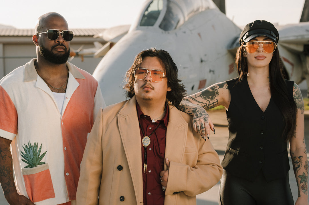 Three people standing in front of an airplane wearing sunglasses with a polished gold frame and amber lenses.