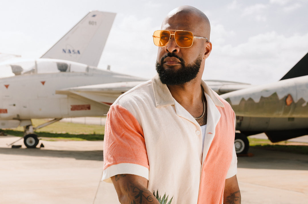 Man wearing sunglasses and a two tone shirt in front of a F-14 airplane