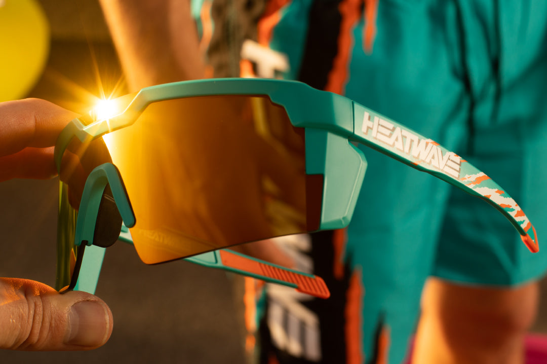 Hand holding Heat Wave Visual Future Tech Sunglasses with teal frame and orange red lens.