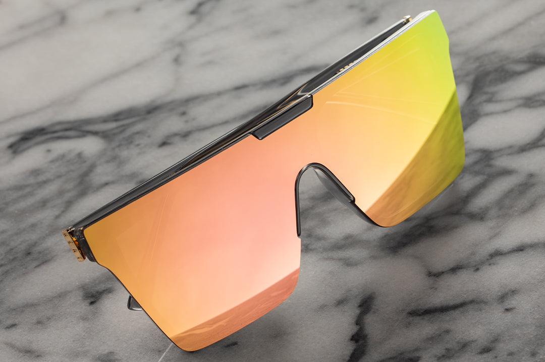 The Heat Wave Visual Clarity Sunglasses with quartz frames and rose gold lens lying on a slab of marble. 