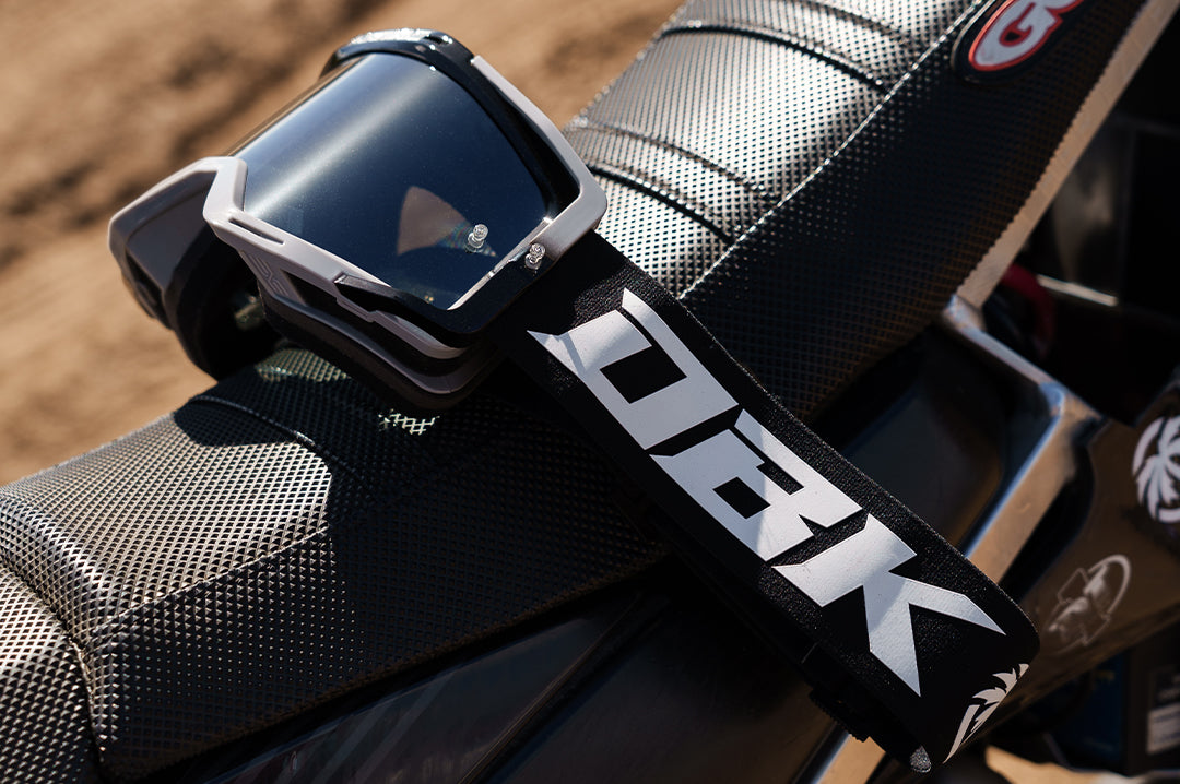 Laying on a dirt bike is the Heat Wave Visual x DBK MXG-250 Moto Goggles. 