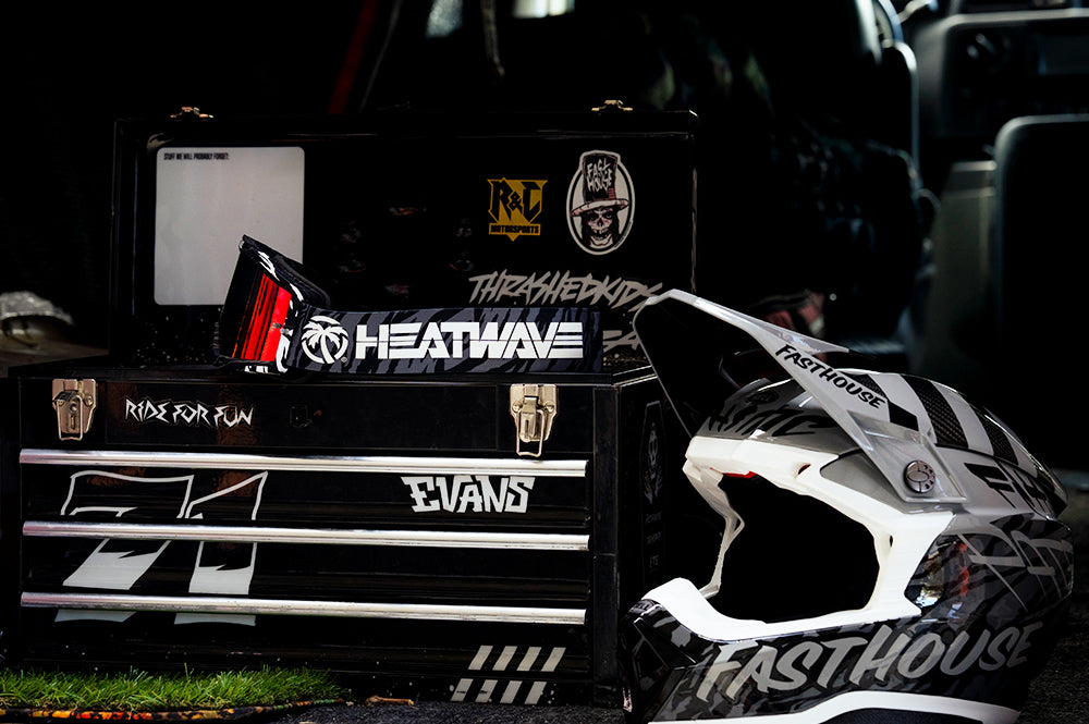 Sitting on top of a tool box is the Heat Wave Visual MXG 250 Motorsport Goggles in the Patrick Evans zebra stirpe color with firestorm red lens.