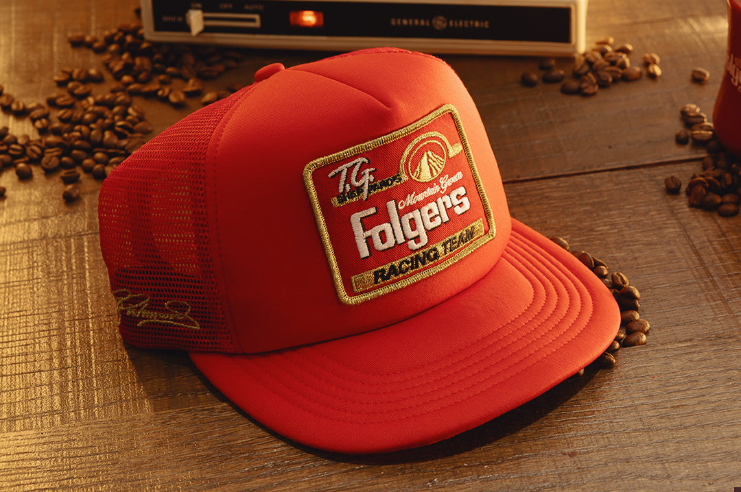 3/4 angle of the HWV Trucker Hat: Hendrick Motorsports | Tim Richmond 25 Folgers on a wood table