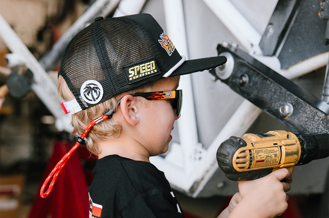 Young boy holding a tool wearing the Little Trouble X Heat Wave Youth Trucker Hat.