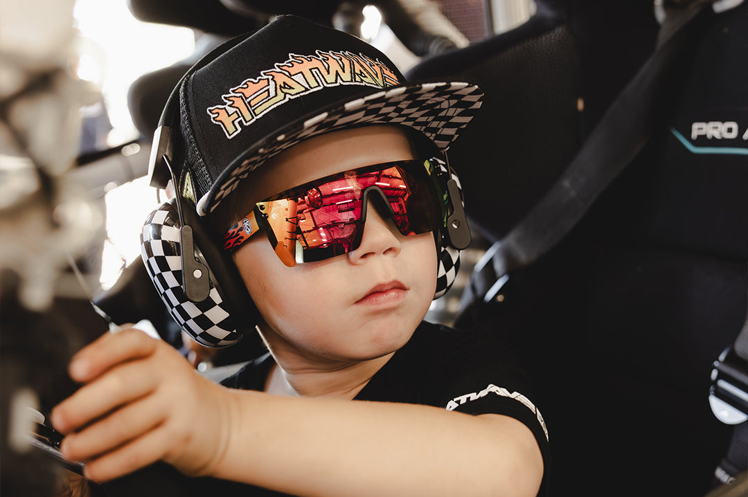 Young boy wearing the Little Trouble X Heat Wave Youth Trucker Hat sitting in a car with their hands on the wheel.