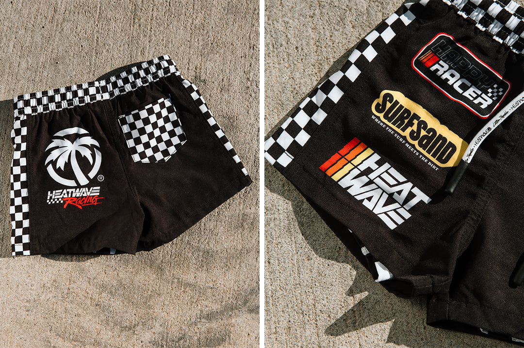 Front and backside of the Little Trouble X Heat Wave Kids Board Shorts on a concrete floor.