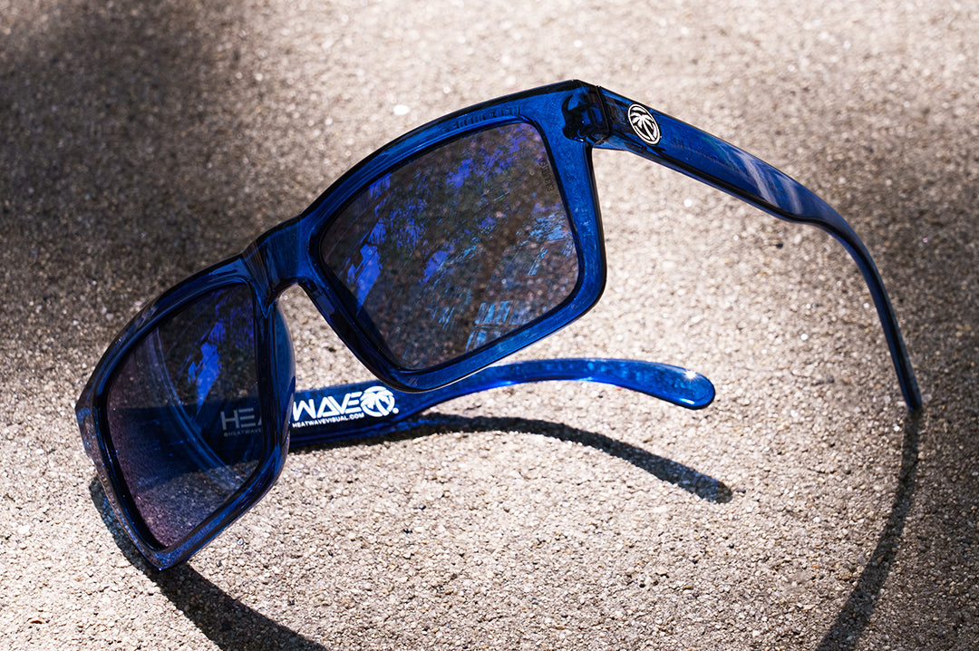 Laying on the floor is the Heat Wave Visual XL Vise Sunglasses with neon blue frames and coastal blue lens.