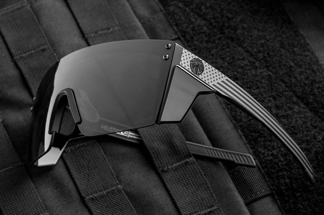 Close up of Heat Wave Performance Lazer black safety glasses with Socom USA Flag arms with bullet proof vest behind them.