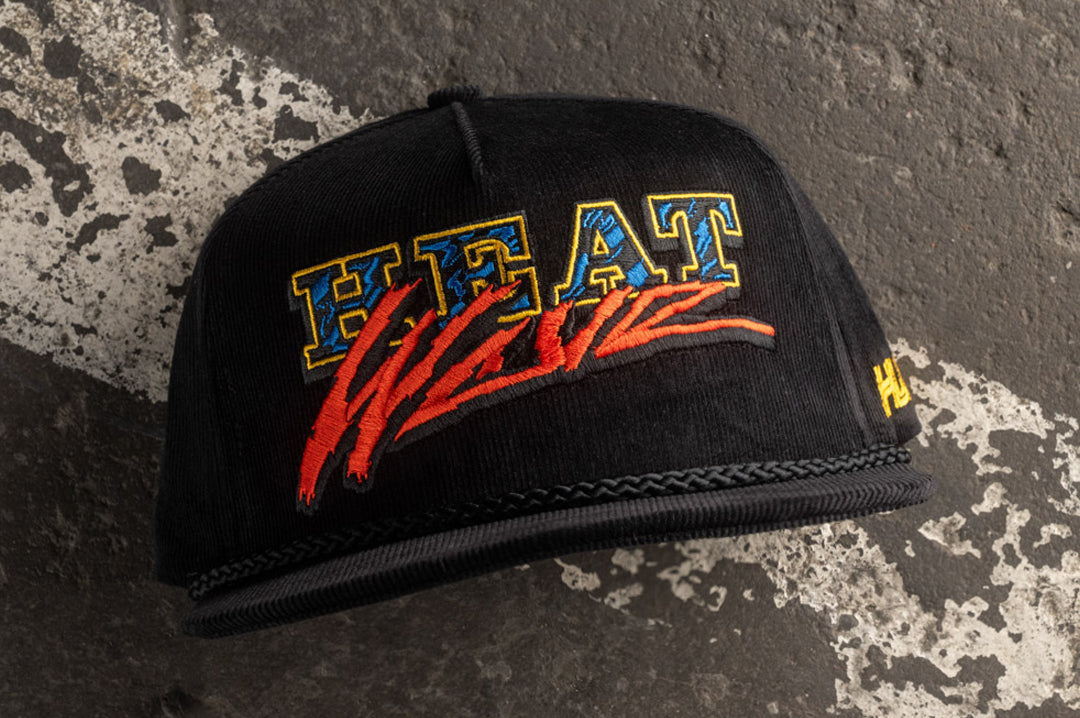 Lying on the concrete ground is the Heat Wave Visual Black Magic Black Cord Hat.