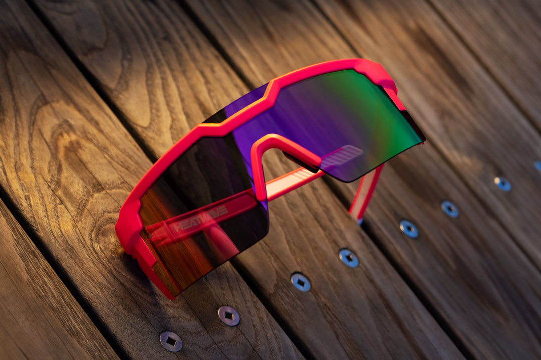 Heat Wave Visual Future Tech Sunglasses with pink frames, standup arms and spectrum pink yellow lens lying on a wooden table. 