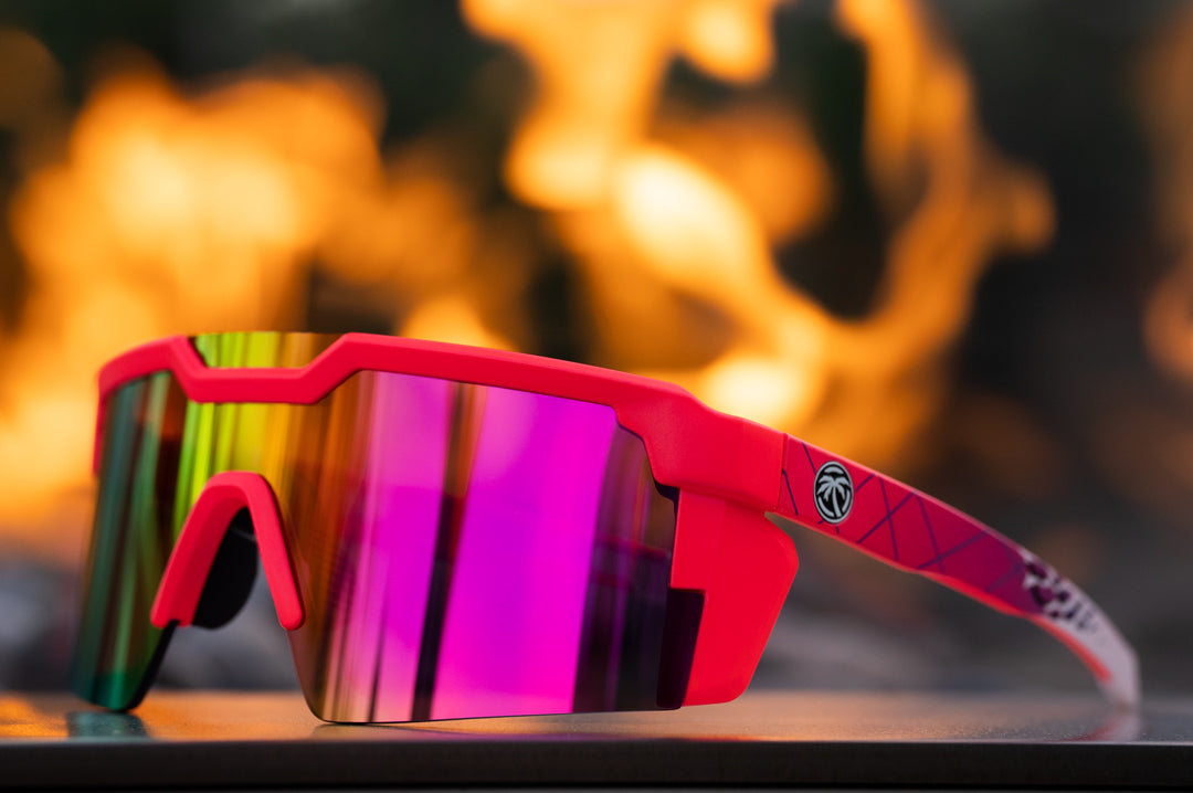 Lying on a table is the Heat Wave Visual Future Tech Sunglasses with pink frame, standup print arms and spectrum pink yellow lens.