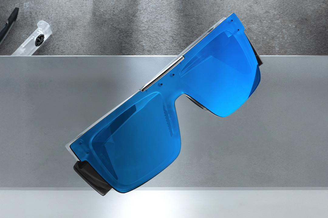 Indoor studio shot of the Performance Quatro Sunglasses: Vapor Frost Frame Coastal Lens Z87+ with blue side shields on a concrete block.