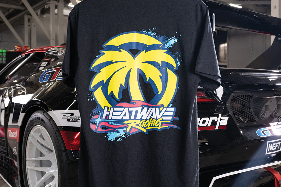 The Heat Wave Y2K Racing Black T-Shirt in front of a car