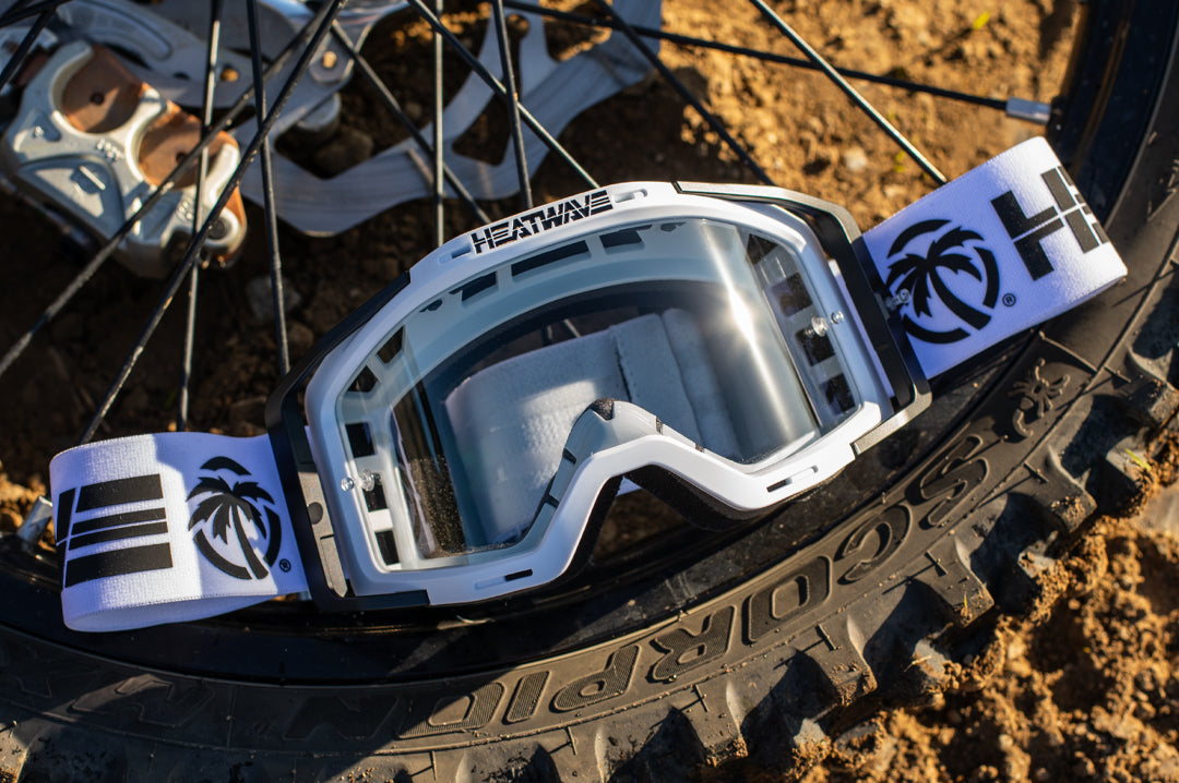 Lying on a dirt bike tire is the Heat Wave Visual MXG 250 Motosport Goggle in the billboard icon white with photochromic lens.