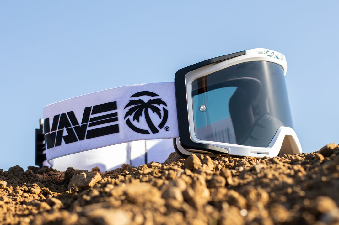 Sitting on a mount of dirt is the Heat Wave Visual MXG 250 Motosport Goggle in the billboard icon white with photochromic lens.