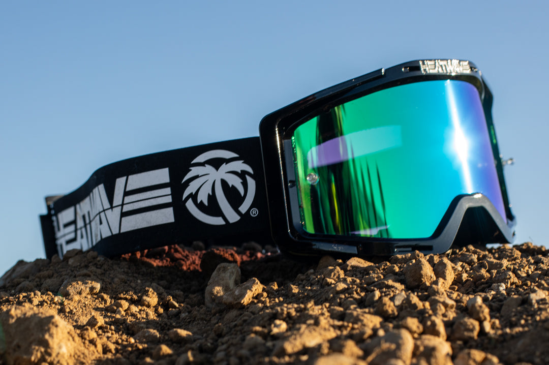 Sitting on a dirt mound is the Heat Wave Visual MXG 250 Motosport Goggle in the billboard icon black with piff green blue lens.