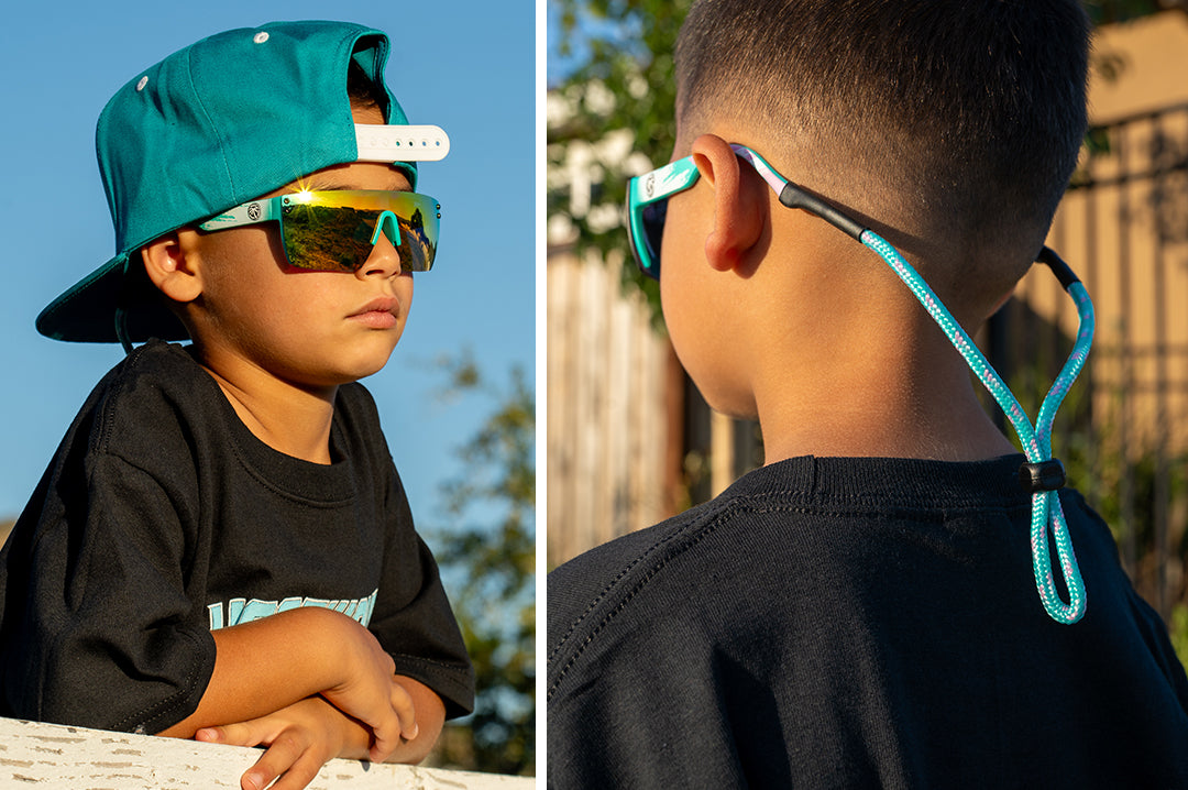 Young kid wearing the Heat Wave Visual Lazer Face Kids Sunglasses with teal frame, brush print arms and spectrum pink yellow lens.