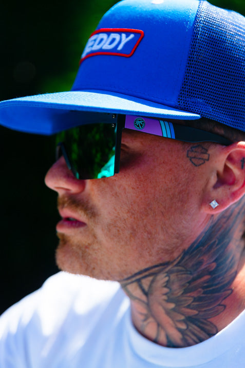 Young guy wearing the Heat Wave Visual Lazer Face Sunglasses with black frame, shreddy bug print arms and ultra violet lens.