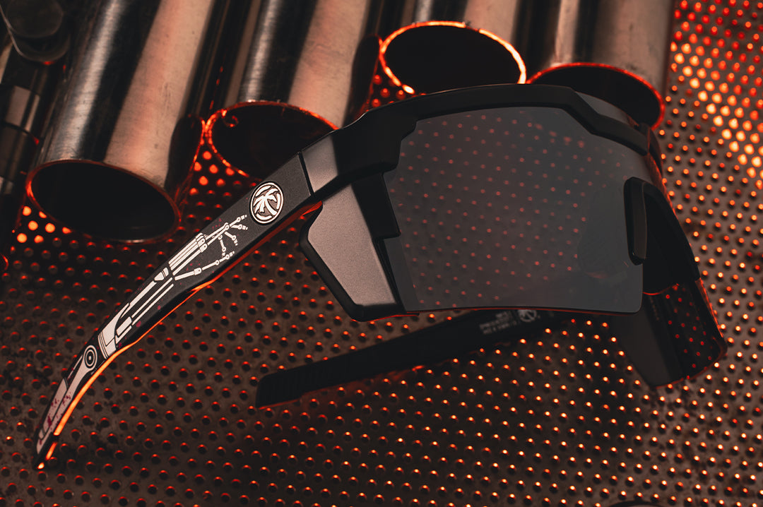 Laying on a metal table is the the Heat Wave Visual Future Tech Sunglasses with black frame, tech noir print arms and silver lens. 