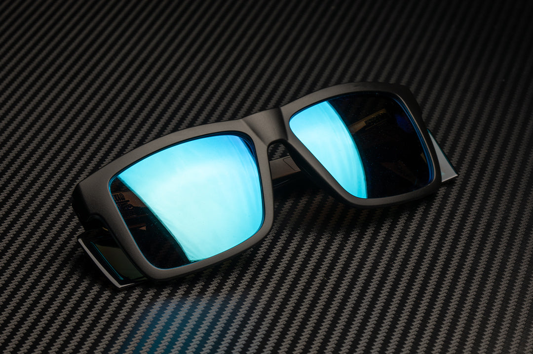 Laying on the Heat Wave Visual Peformance Vise Sunglasses with black frame and galaxy blue lenses.