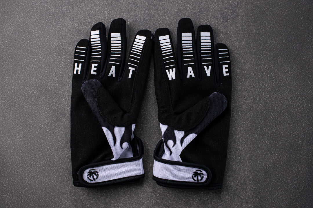 Lying on the concrete floor is the Heat Wave Visual White Flame Moto Gloves. 