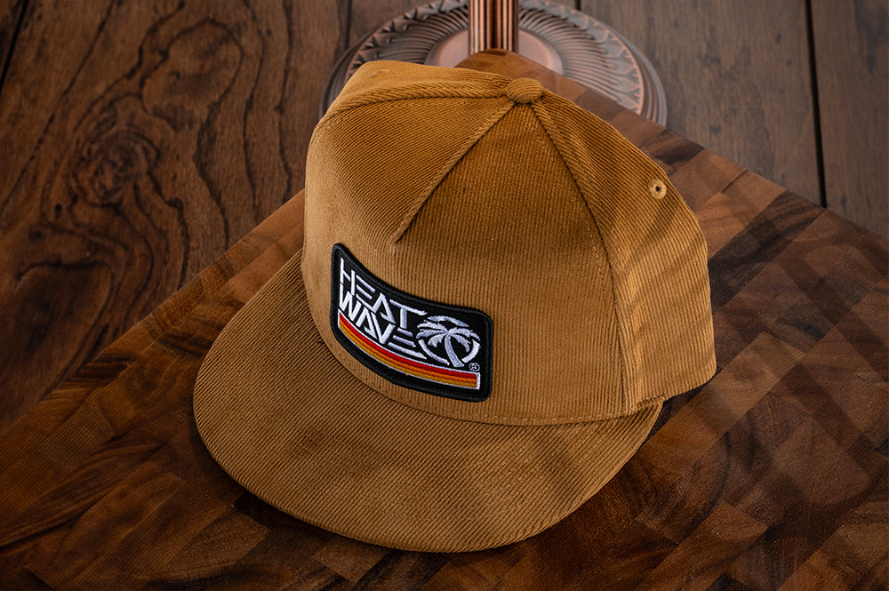 Lying on a wooden table is the Heat Wave Visual Retro Stripe Brown Hat.