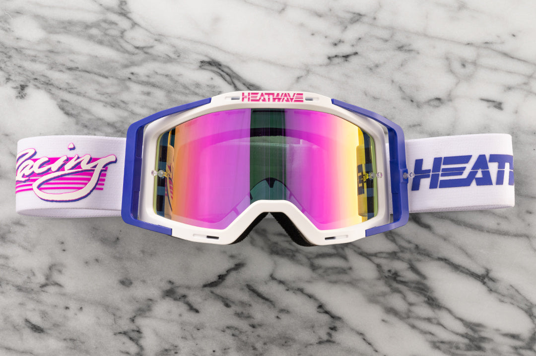 Lying on a marble counter top is the Heat Wave Visual MXG 250 Motorsport Goggles in the Highlighter Racing white color with spectrum pink lens.