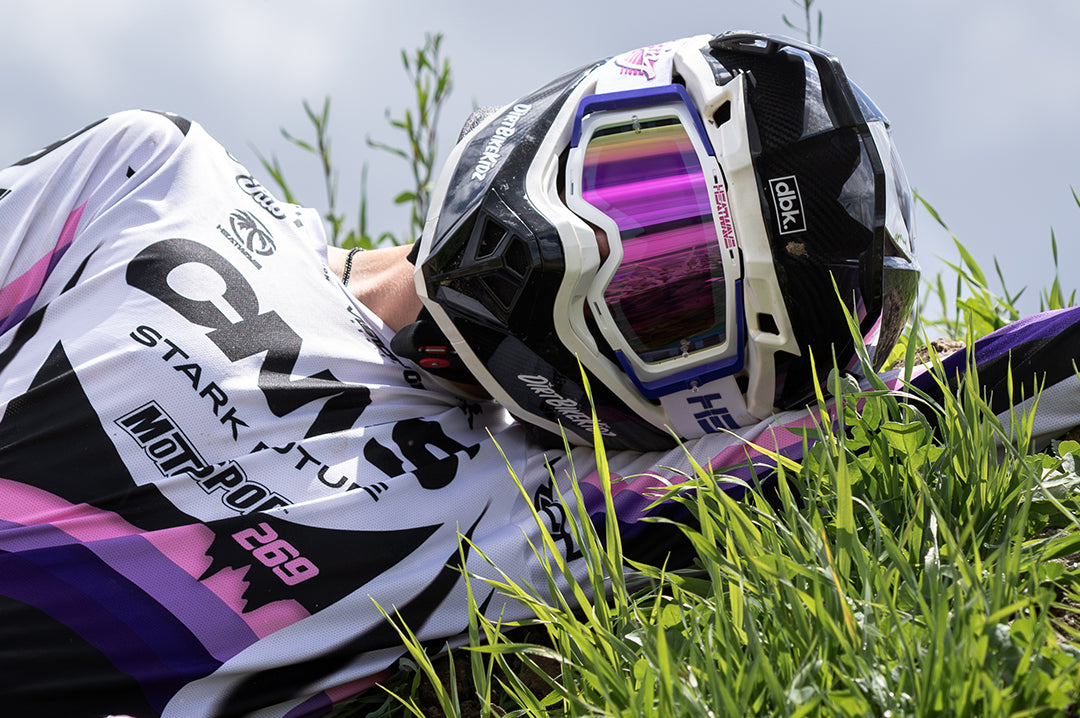 Ryan Ritter lying on the floor wearing the Heat Wave Visual MXG 250 Motorsport Goggles in the Highlighter Racing white color with spectrum pink lens.