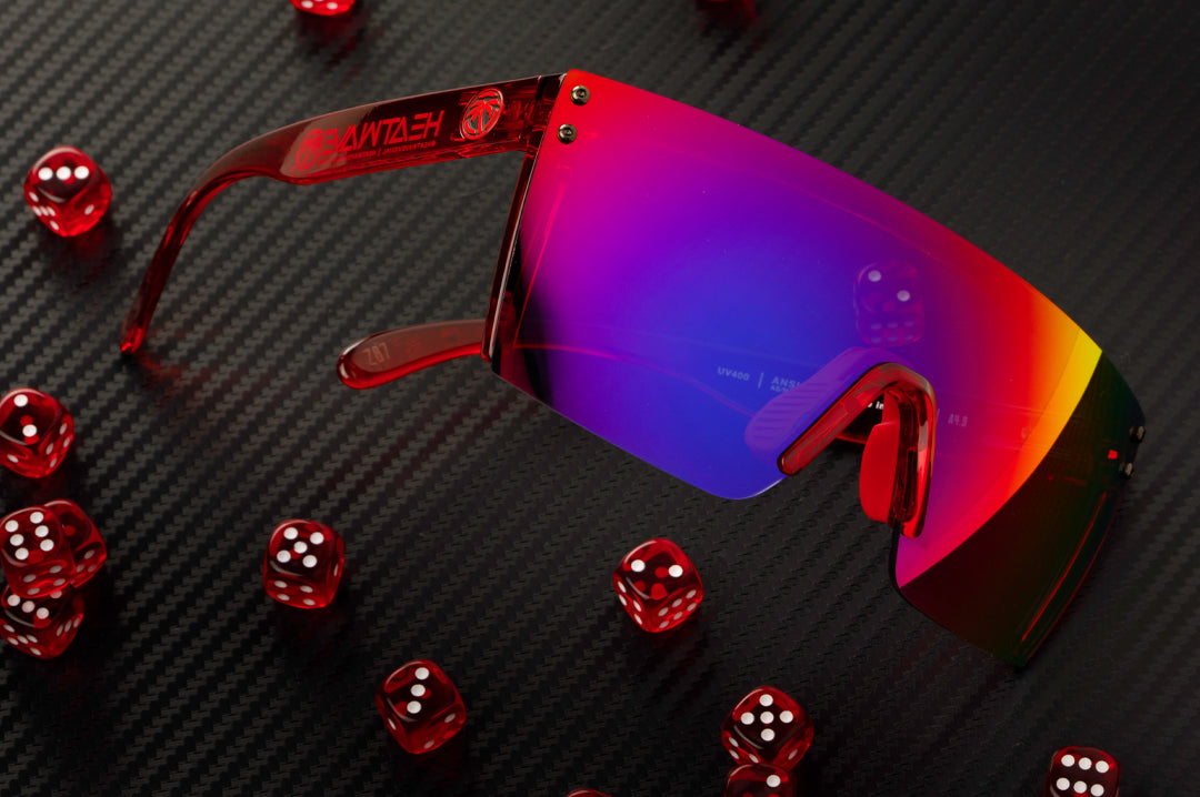 Laying on a table with red dice is the Heat Wave Visual Lazer Face Sunglasses with neon red frame and atmosphere blue red lens.